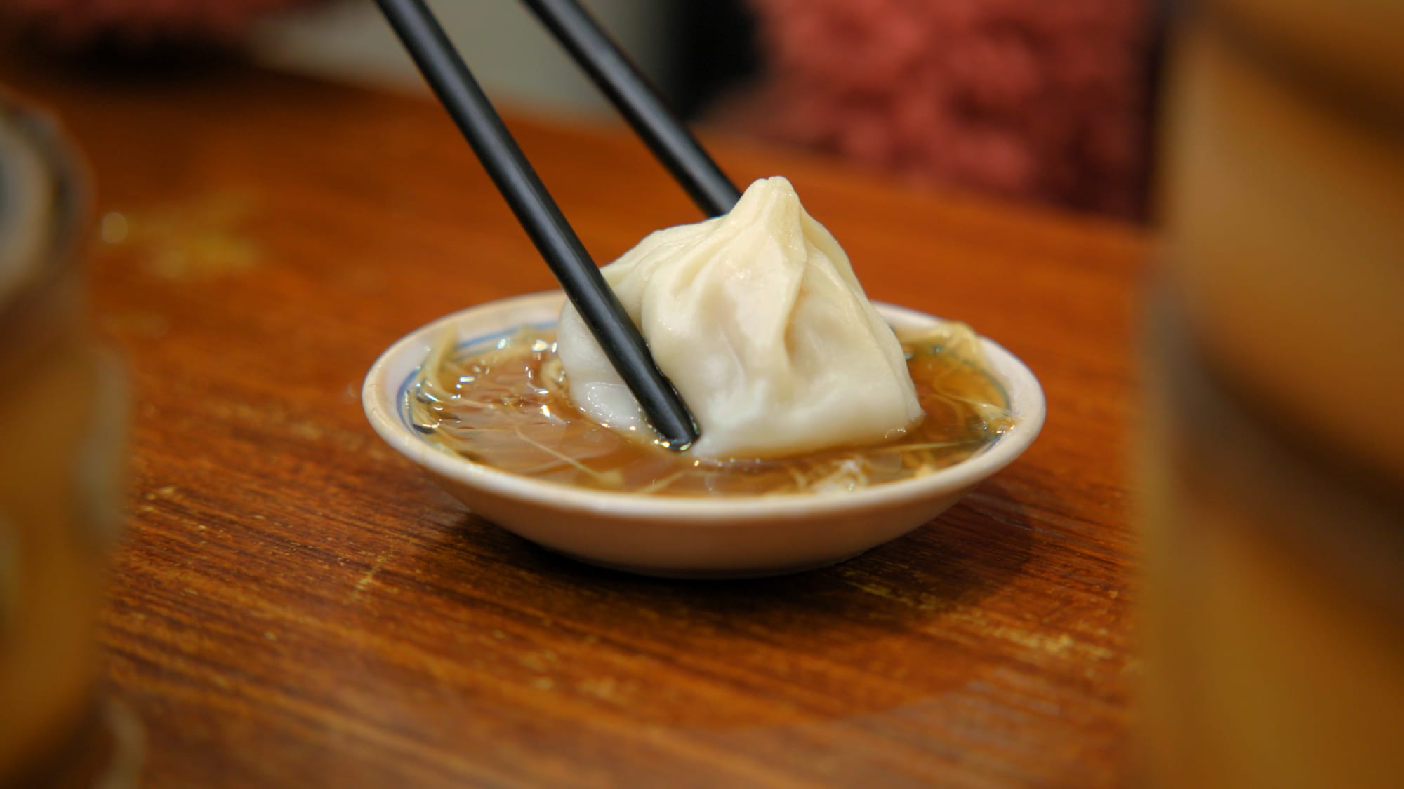 Xiaolongbao being dipped into vinegar with slivers of ginger